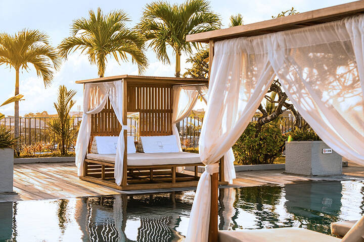 Sunbeds near swimming pool overlook palm trees on beach at Cross Paasha Seminyak Bali