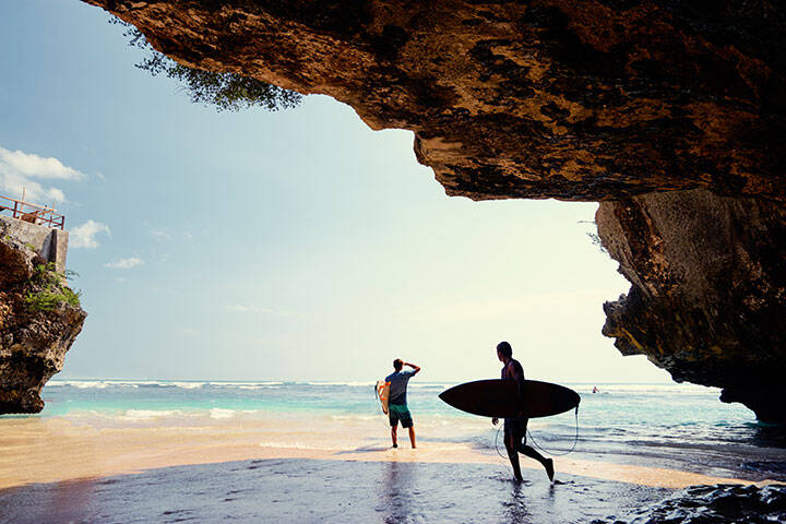 Surfers with surfboard on beautiful beach with high rocks in Uluwatu, Bali, Indonesia.