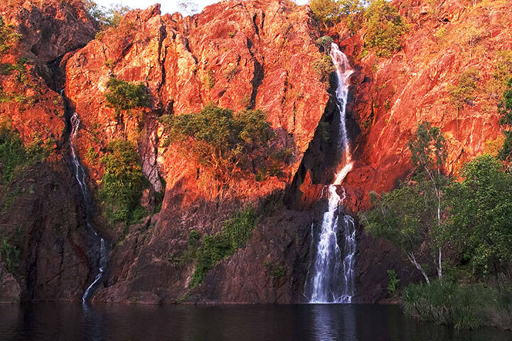 The setting sun turns the cliffs at Wangi Waterfalls in Litchfield National Park a brilliant shade of red 