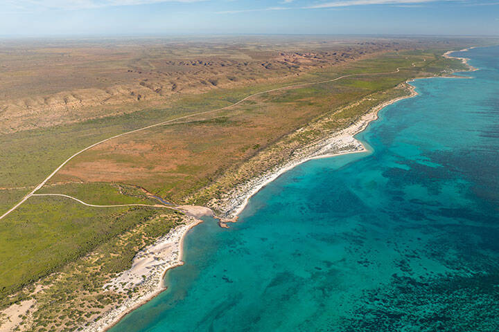 Areal view of the coastline in Cape Range National Park near Exmouth. The turquoise waters meeting the dry yet green bushland next to the rugged ridges of the rang