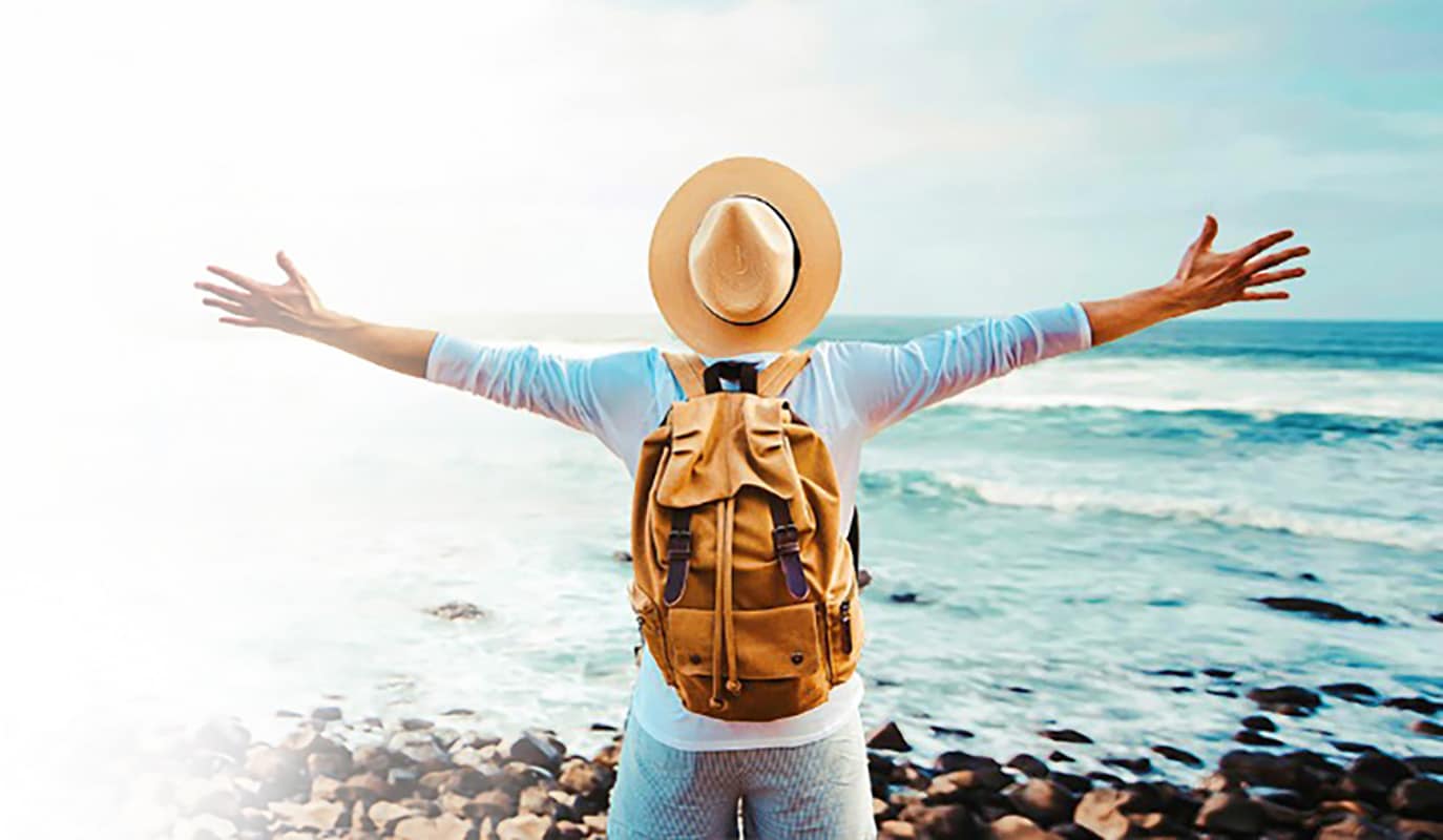 Traveller wearing a backpack and hat staring at the ocean