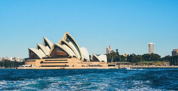 A vibrant shot of the Sydney Opera House set against a bright sunny day, with clear blue skies and the sparkling waters of Sydney Harbour.