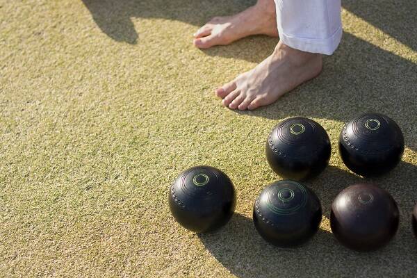 A close-up of a player's feet standing next to lawn bowls on astro turf at a barefoot bowls venue in Sydney.