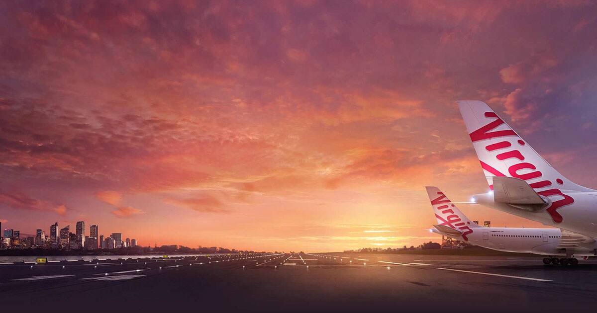 A Virgin Australia plane's tailfin against a vibrant sunset on the tarmac.