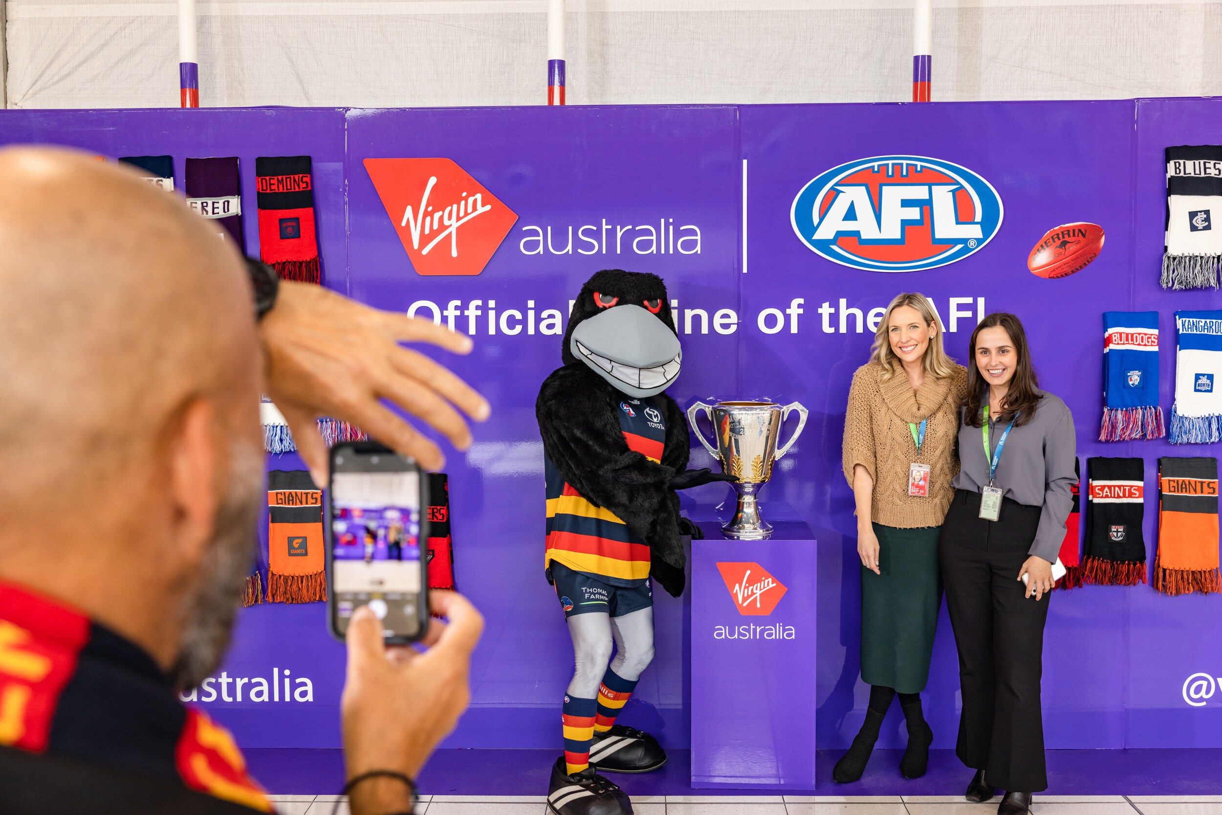 Adelaide Crows fans standing proudly next to the AFL Grand Final trophy