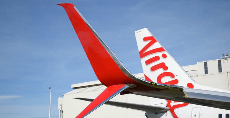 Close up photo of Virgin Australia tailfin against blue sky on tarmac.