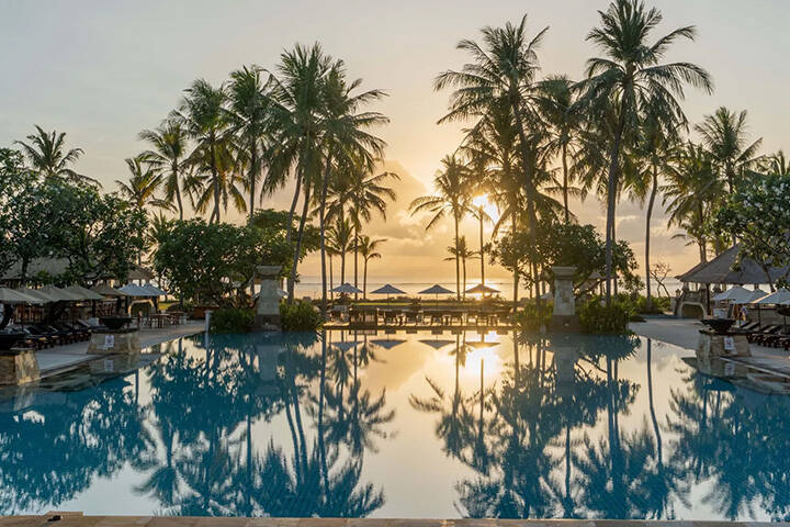 Pool area surrounded by palm trees at sunrise Conrad Bali in Nusa Dua 