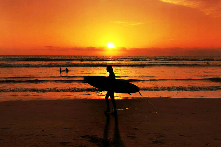 Silhouette of man holding surfboard walking on Kuta beach during sunset 