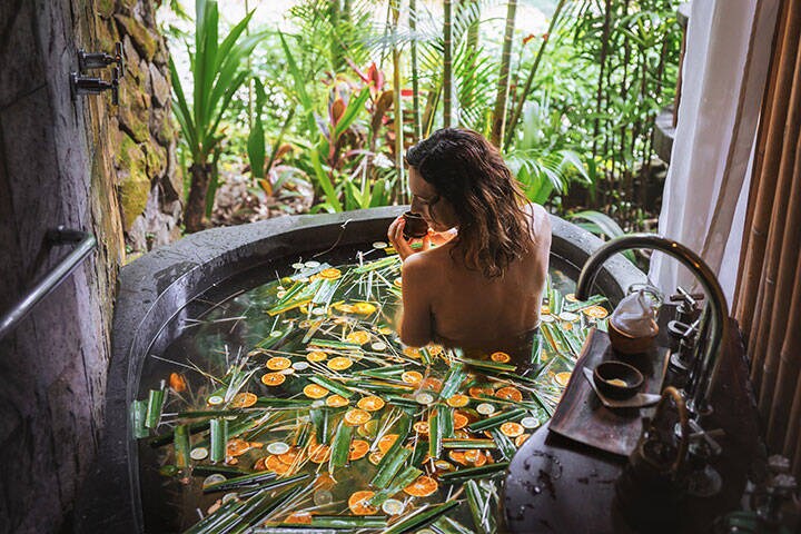 Young woman enjoying in outdoor luxury spa in a stone bath tub with jungle view.