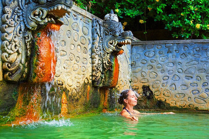 Young woman standing in thermal bath, relaxing under flowing water stream of shower in natural mineral hot spring Banjar during a day tour on family holidays