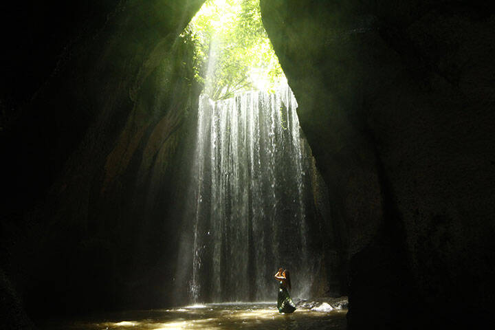 Model in green dress praying in Tukad Cepung waterfall, Bali, Indonesia