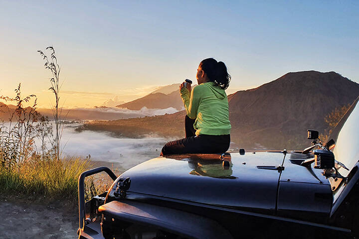 Woman sit on car hood while enjoy mount batur view 