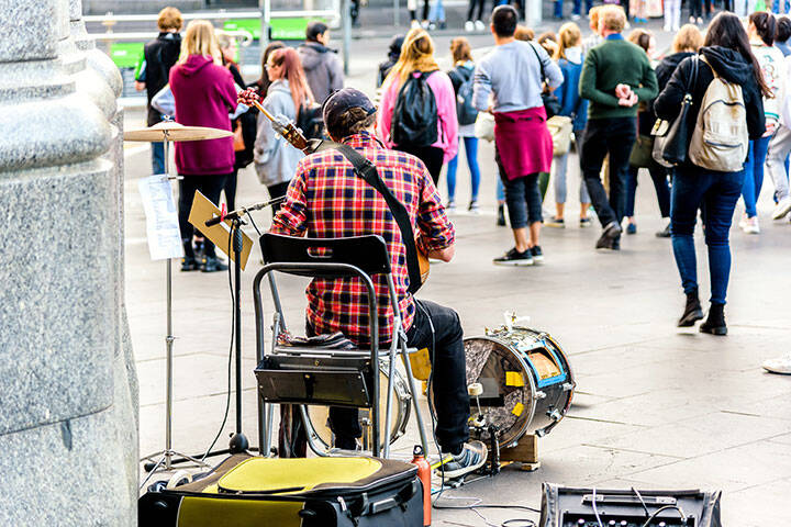 A solo busker is sitting in front of the Flinders Street Train Station 