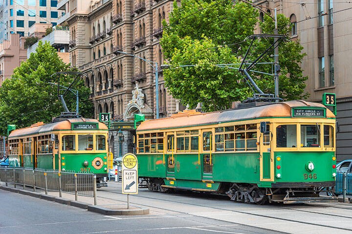 A pair of Melbourne city trams are at the Spring Street tram stop in front of the Windsor Hotel 