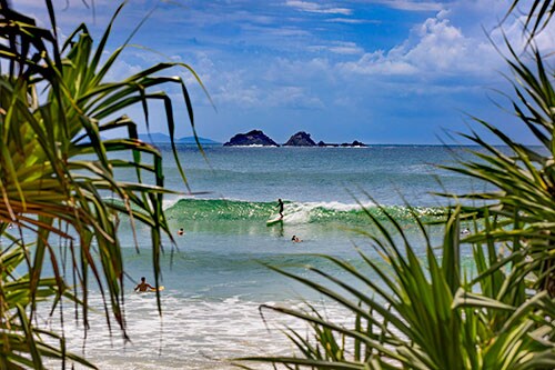 Surfers catching waves off Watgos Beach in Byron Bay with views across to Julian Rocks. Credit: Destination NSW