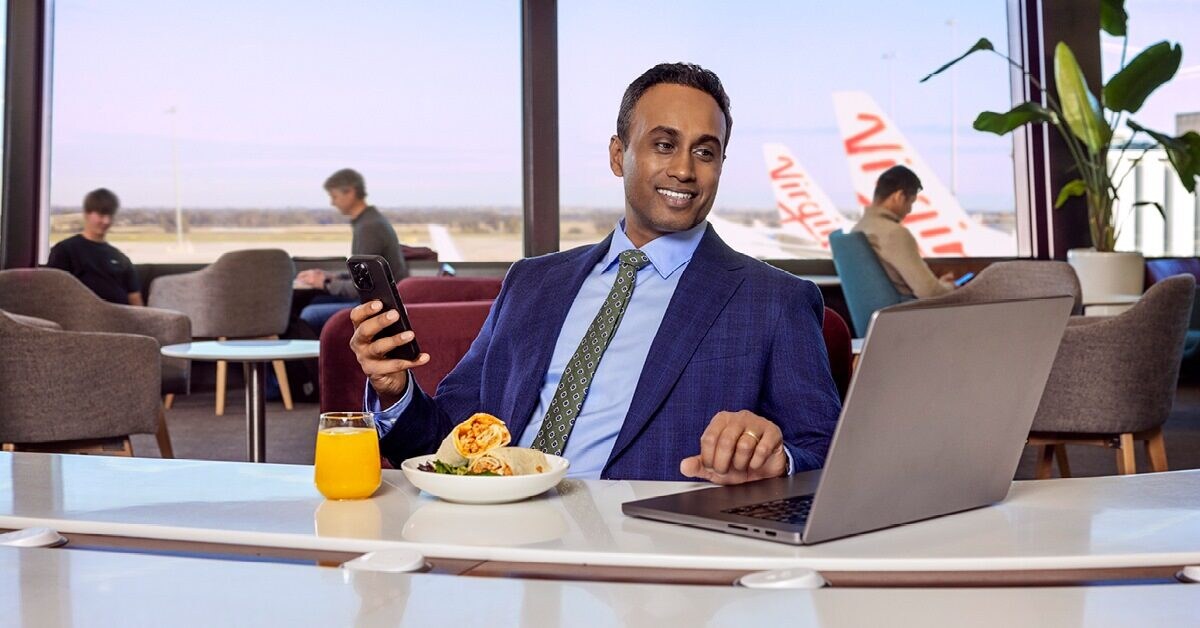 Businss map sitting at the airport lounge, with his laptop and food in front of him, phone in hand.