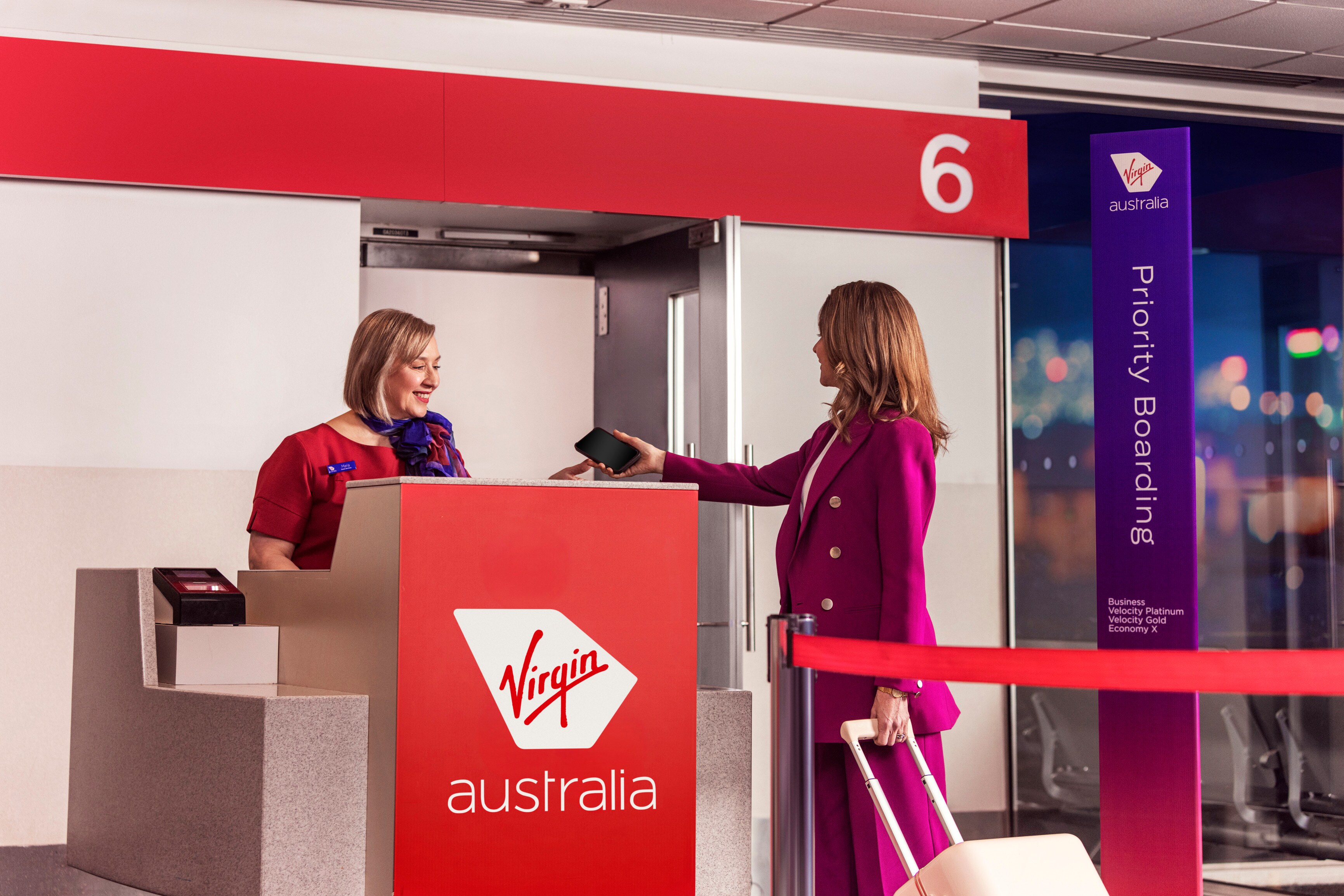 Woman traveling internationally for work handing her smartphone to a Virgin Australia worker at the priority boarding gate